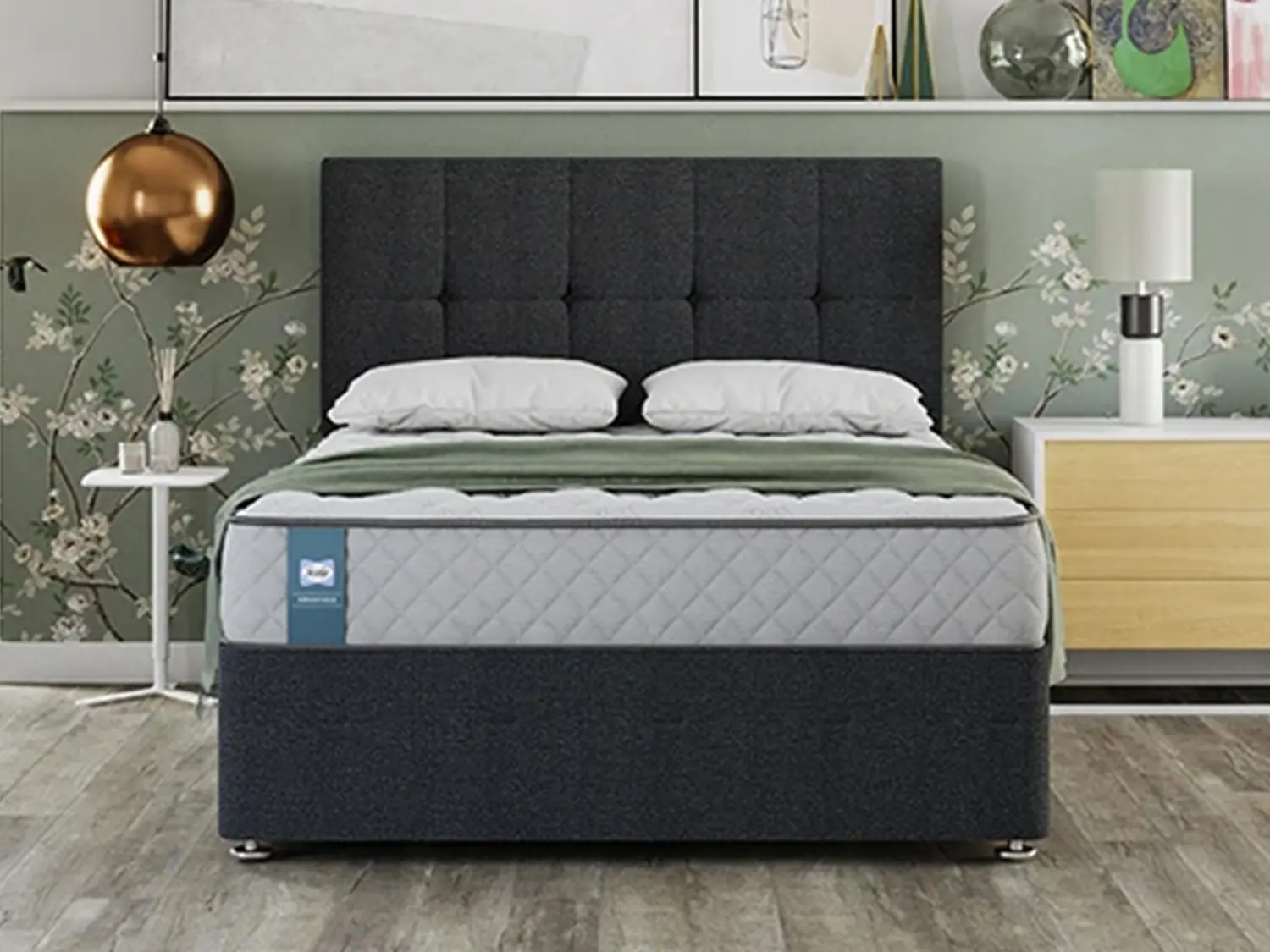 Sealy Advantage Alford mattress featuring a quilted side border, styled on a dark charcoal tufted divan bed in a room with floral wallpaper.