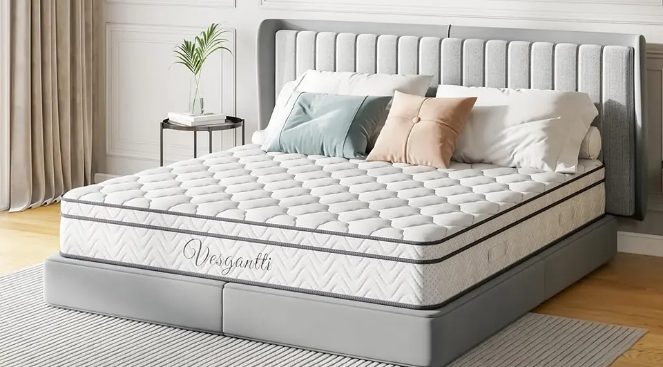 A Vesgantti pocket sprung hybrid mattress with a white tufted pillow-top and grey breathable side mesh, styled on a modern grey upholstered bed frame in a bright, minimalist bedroom.